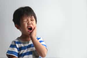 A young boy holding his cheek in pain for toothache