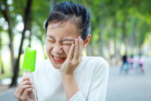 Asian child girl holding her hand on her aching tooth have hypersensitive teeth eating ice cream