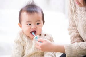 A mother holding a toothbrush and brushing her infants teeth