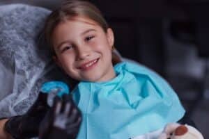 A girl sitting in a dental chair with a mouthguard shown by the dentist