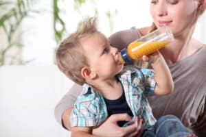 Child,Drinking,Juice,In,His,Mother's,Lap