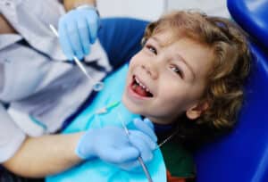 Young boy smiling while getting dental treatment to repair cavities to his baby teeth.